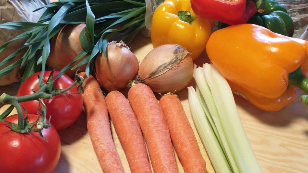 Vegetables on a counter: tomatoes, peppers, onions, carrots, celery